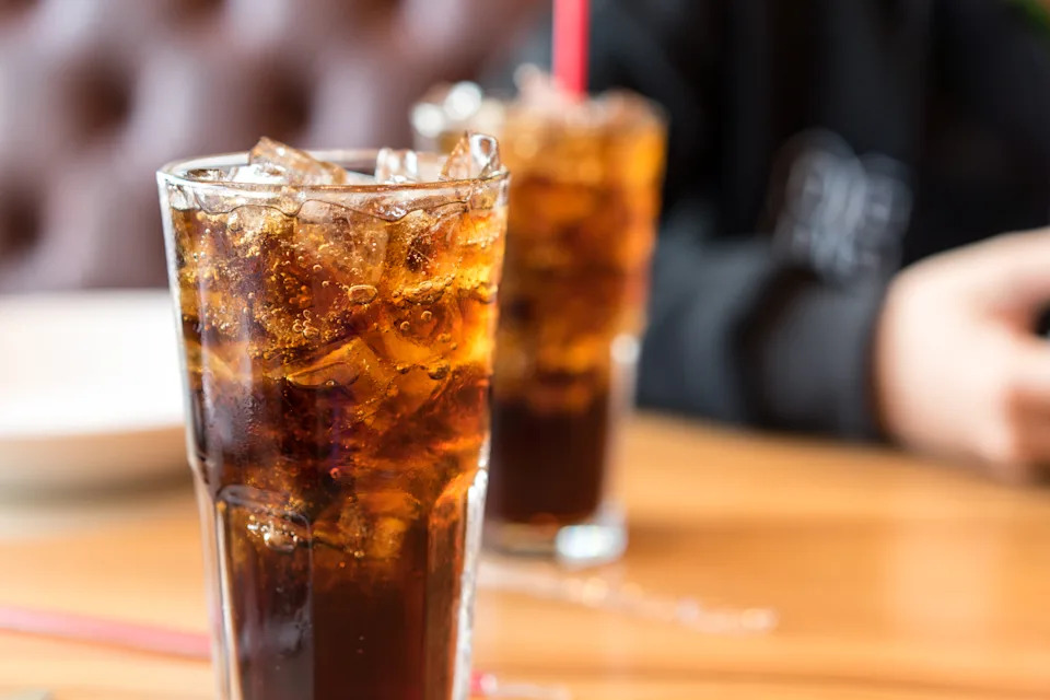 Two glasses of iced soda on a wooden table, with a frosted exterior that gives the impression of a casual dining area.