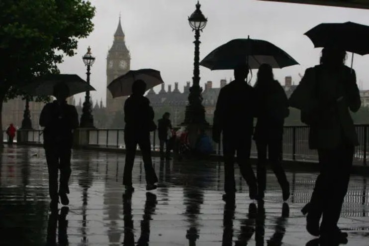 A rainy and gloomy British landscape with overcast clouds, wet streets, and people holding umbrellas in a busy city.