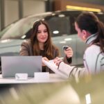 A woman is sitting in a car showroom talking to a salesperson.