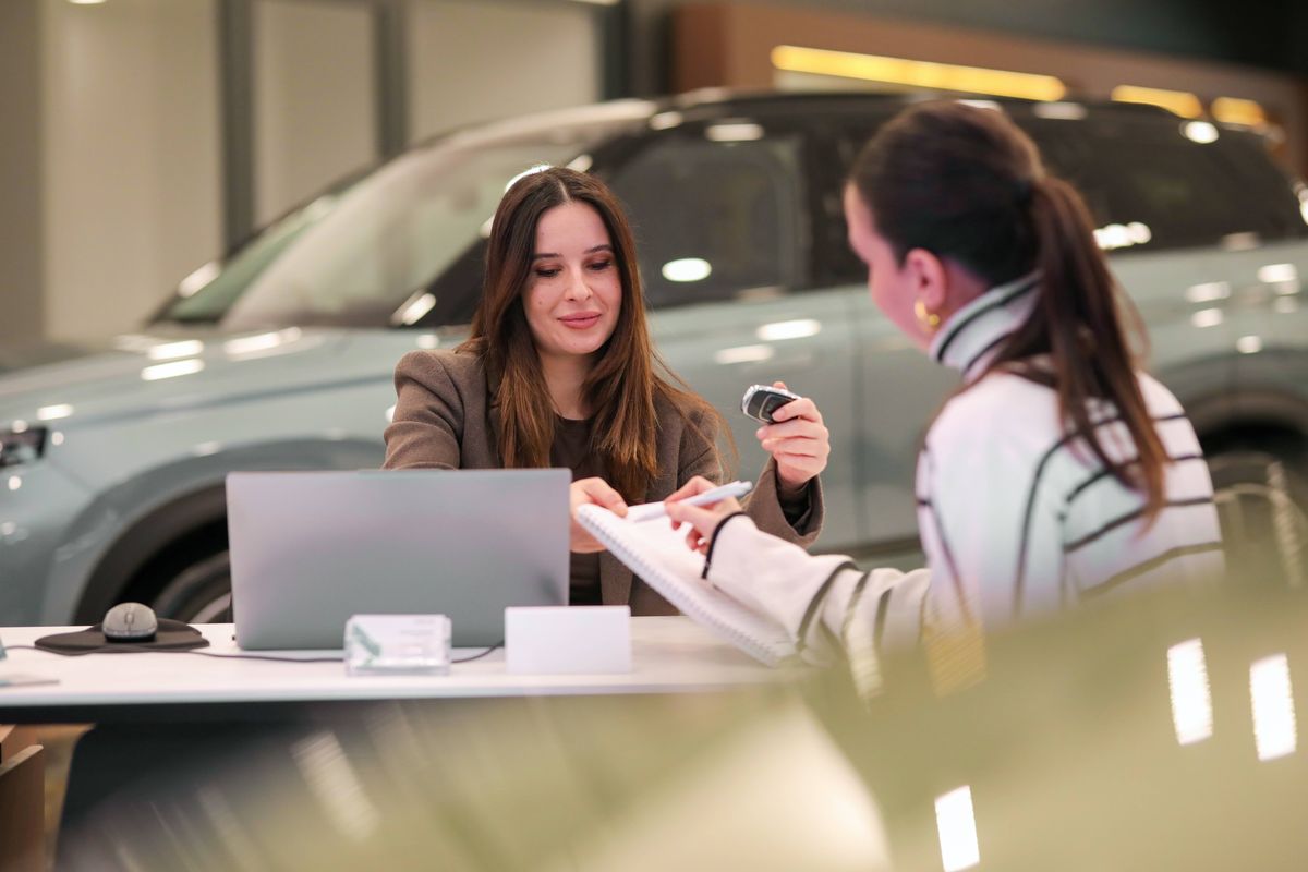 A woman is sitting in a car showroom talking to a salesperson.