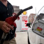 A man is holding a can of petrol next to his car.