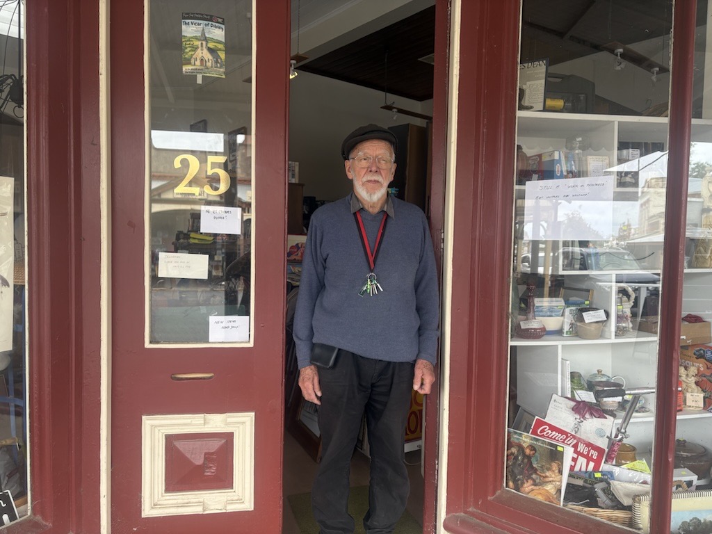 A man with a white beard and a flat cap at the door of the bookstore. 