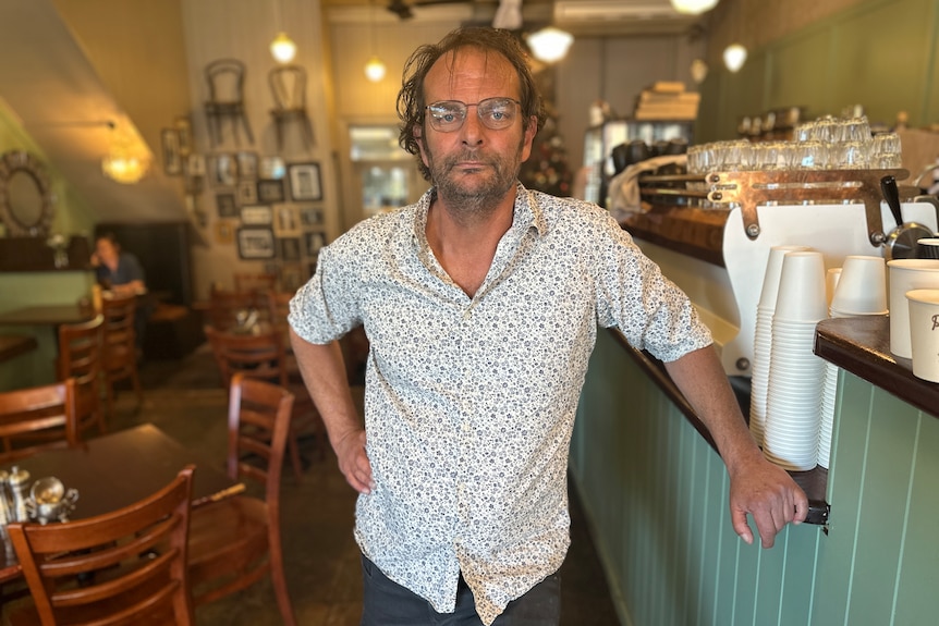 A man in a white shirt looks at the camera in his cafe.