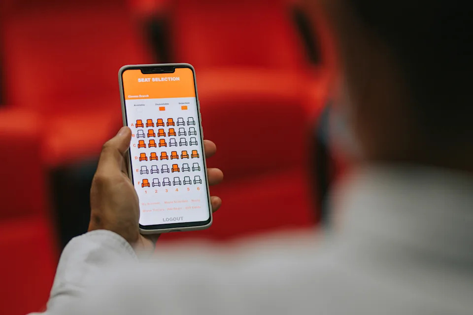 A person is holding a smartphone showing a seat selection screen in a theater