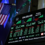 Stock market board showing Doe Jones and other green and red stocks next to the US flag.