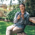 A woman sitting on a bench outside holding a mug.