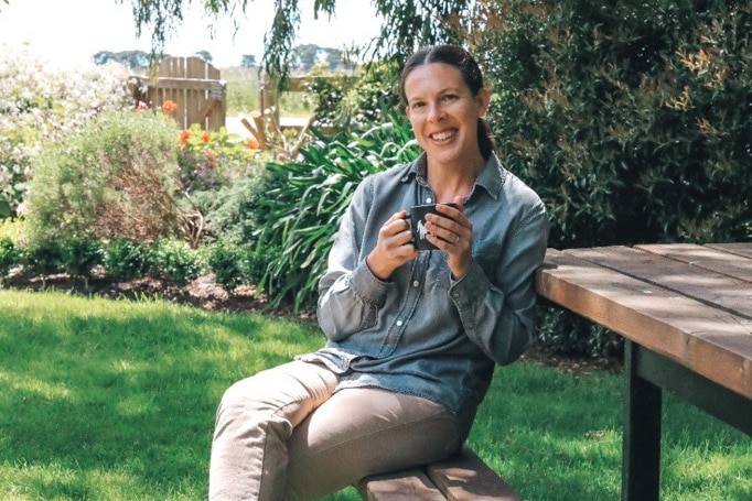 A woman sitting on a bench outside holding a mug.
